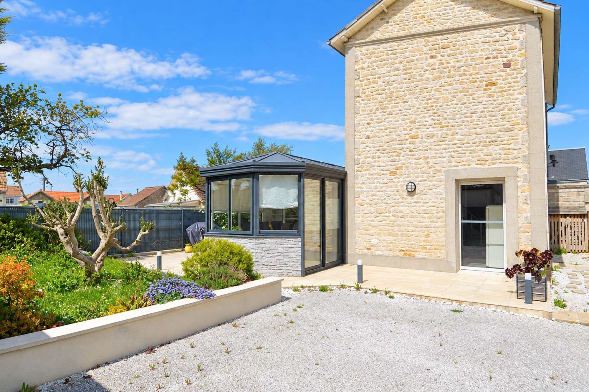 A modern house with a stone facade, a glass conservatory, and a gravel driveway.