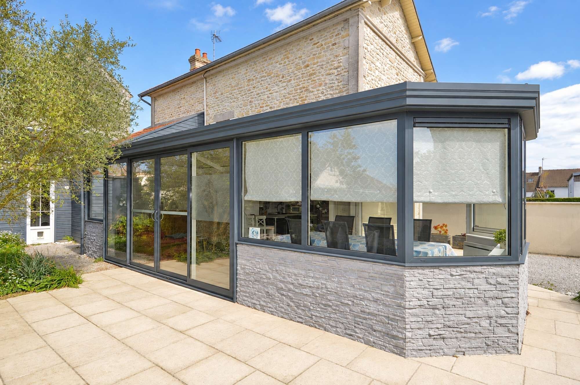Ein modernes Haus mit einer großen Glasfassade, Steinmauern und einer gepflasterten Terrasse.