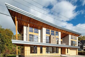 A modern two-story house with a balcony, large windows, and a wooden facade.