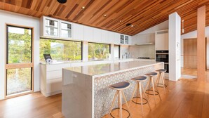 A modern kitchen with a large island, bar stools, and a view of the outdoors. - Ro-An (Kutchan)