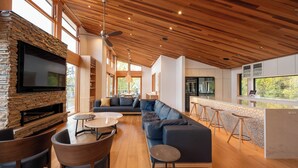 A modern living room with a stone fireplace, a large flat-screen TV, a sectional sofa, and a dining area with round tables. - Ro-An (Kutchan)