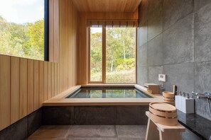 Ein modernes Badezimmer mit einer gläsernen Whirlwanne, Holzdetails und Blick auf Bäume.