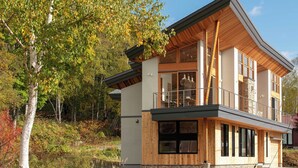 A modern two-story house with a balcony, large windows, and a stone foundation. - Ro-An (Kutchan)