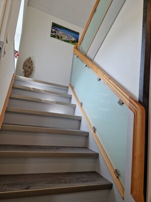 Un escalier avec des rampes en bois et des panneaux de verre, menant à un palier agrémenté d’un élément décoratif mural.