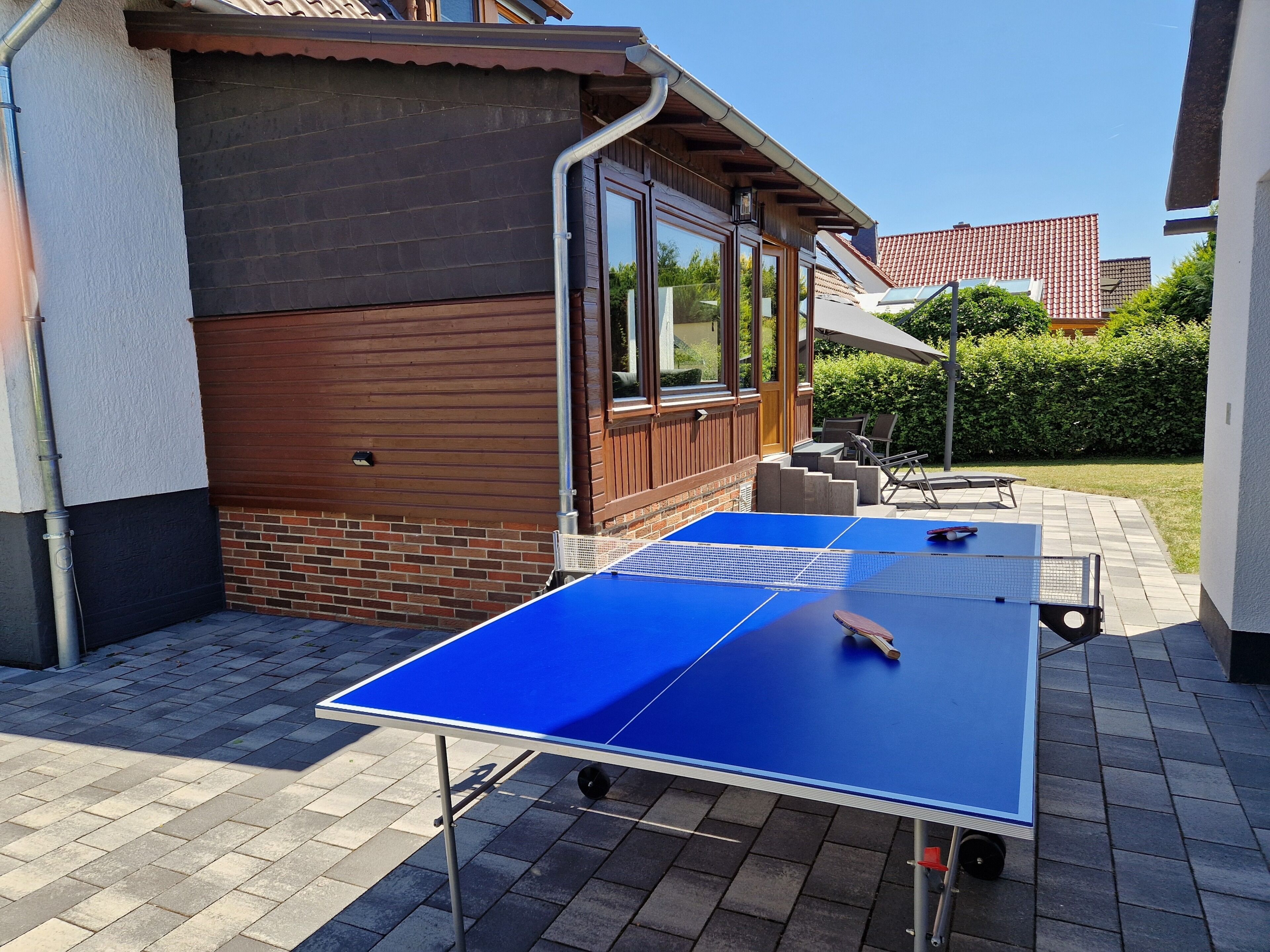 A blue ping pong table in an outdoor patio area with a brick wall and wooden paneling.