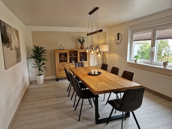 A dining area with a wooden table, black chairs, a cabinet with glass doors, a hanging light fixture, and a window with blinds.