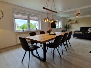 Un espace repas avec une table en bois, des chaises noires et des luminaires suspendus.