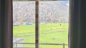 Una ventana con vistas a un campo verde, algunos edificios y una montaña al fondo.