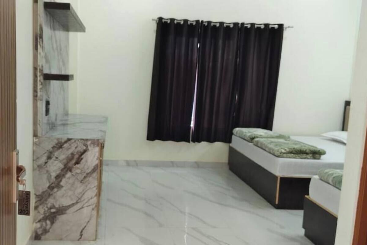 Una habitación con encimera de mármol, una cama con manta verde, una cortina negra y un panel de madera a la izquierda.