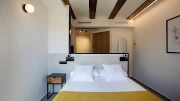 A modern hotel room with a large bed, a bedside table, a mirror, and a framed artwork on the wall.