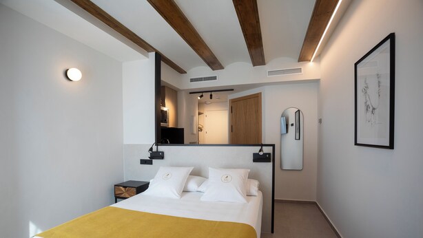 Una habitación de hotel moderna con cama, mesitas de noche, espejo, una obra de arte enmarco y una viga de techo de madera.