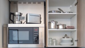 A compact kitchen with a microwave, toaster, and open shelving with dishes and cookware. - Mon Suites Platería (Valencia)