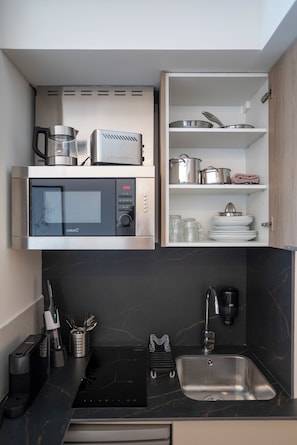 A compact kitchen with a microwave, toaster, and open shelving with dishes and cookware. - Mon Suites Platería (Valencia)