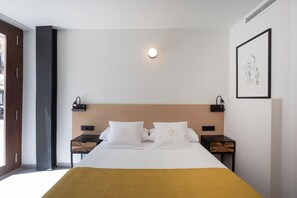 A modern hotel room with a bed, bedside tables, a wall-mounted light, and a framed artwork. - Mon Suites Platería (Valencia)