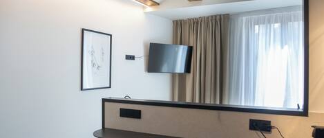 A modern room with a wooden ceiling, a flat-screen TV mounted on the wall, a window with curtains, and two stools at a counter.