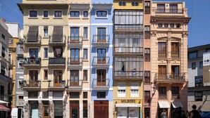 A row of multi-story buildings with balconies, a visible storefront, and a cobblestone street. - Mon Suites Platería (Valencia)
