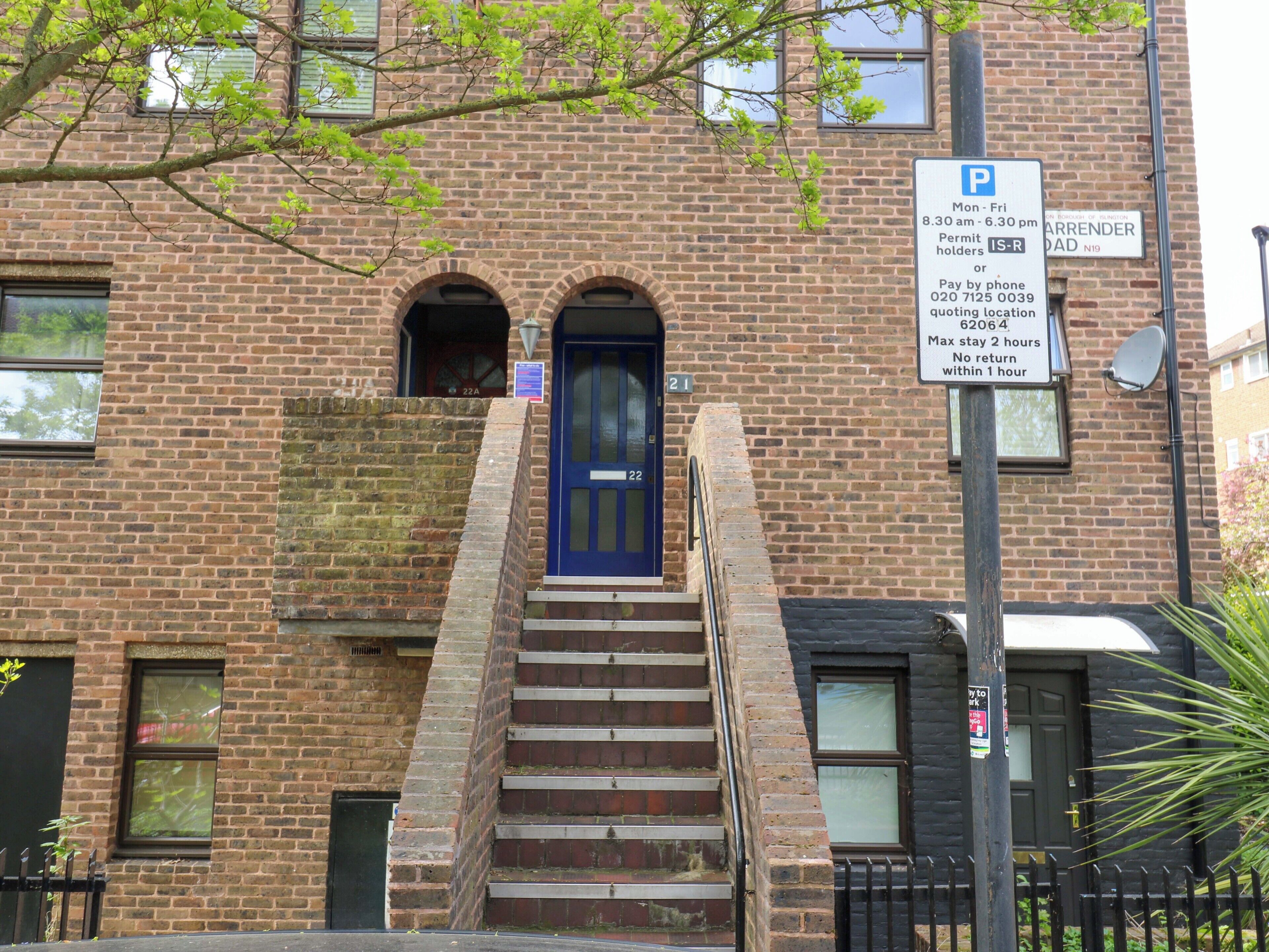 A brick building with a blue door, a parking sign, and a staircase leading to the entrance.