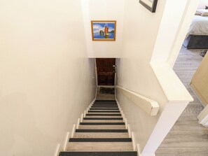 Een trap met houten treden en witte trapleuning, die leidt naar een kamer met een bed en een lijst met een afbeelding erop.