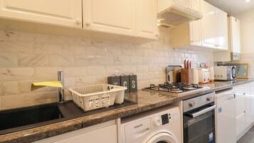 A modern kitchen with white cabinets, a built-in washing machine, a stove, and a microwave.