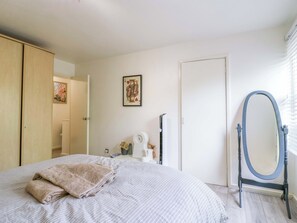 Een slaapkamer met een bed, een spiegel, een deur en een aan de muur hangend schilderij.