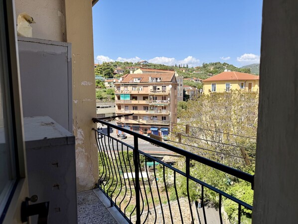 Ein Balkon mit Metallgeländer, der auf einen Wohnbereich mit mehrstöckigen Gebäuden und einem wolkenlosen Himmel blickt.