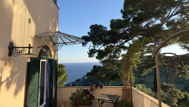 A balcony with a view of the sea, a table, and a potted plant. - Tery’s Apartment (Imperia)