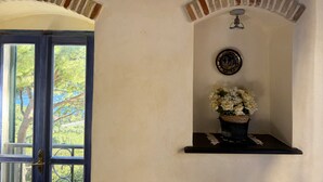 A room with a door leading outside, a wall-mounted shelf with a vase of flowers, and a ceiling fan. - Tery’s Apartment (Imperia)