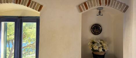 A room with a door leading outside, a wall-mounted shelf with a vase of flowers, and a ceiling fan.