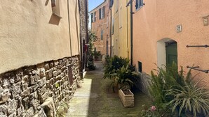 A narrow street with stone walls and buildings with shutters and signs. - Tery’s Apartment (Imperia)
