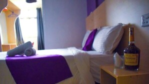 A hotel room with a bed, a nightstand, a bottle of alcohol, and a window with curtains. - LIAZONS HOTEL NAKURU (Nakuru)