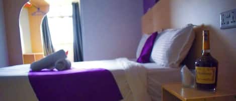 Una habitación de hotel con una cama, una mesita de noche, una botella de licor y una ventana con cortinas.