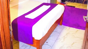 A bedroom with a bed, a bedside table, a chair, a door, and a curtain. - LIAZONS HOTEL NAKURU (Nakuru)