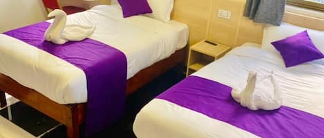 Habitación de hotel con dos camas, cada una con una colcha morada y un adorno de cisne blanco.