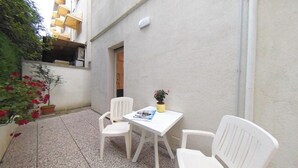 A small outdoor seating area with a table and two chairs, a potted plant, and a building in the background. - Perfectly located flat near the beach and shops (Lignano Sabbiadoro)