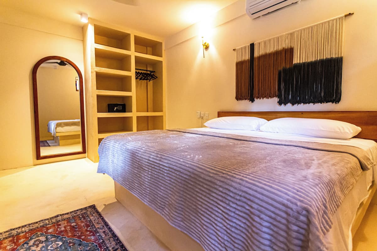 A bedroom with a bed, a wardrobe, a mirror, and a wall-mounted light fixture.