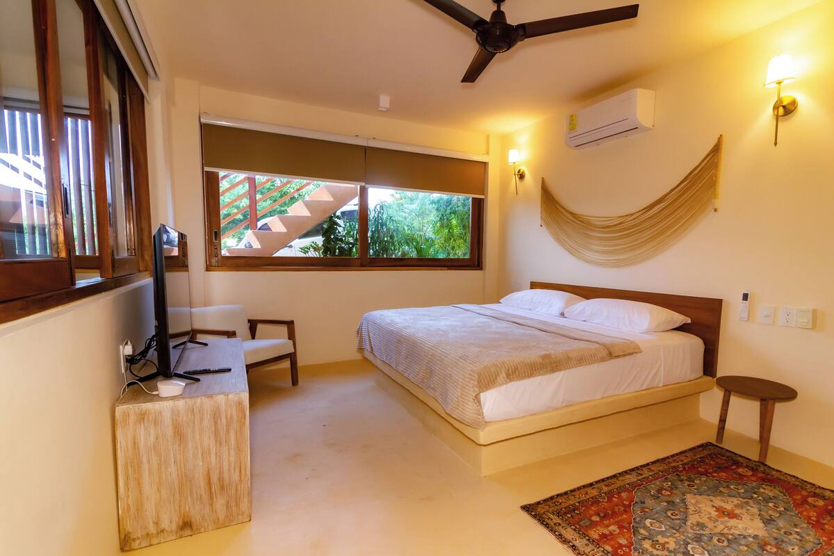A bedroom with a bed, a desk, a chair, a window, and a ceiling fan.