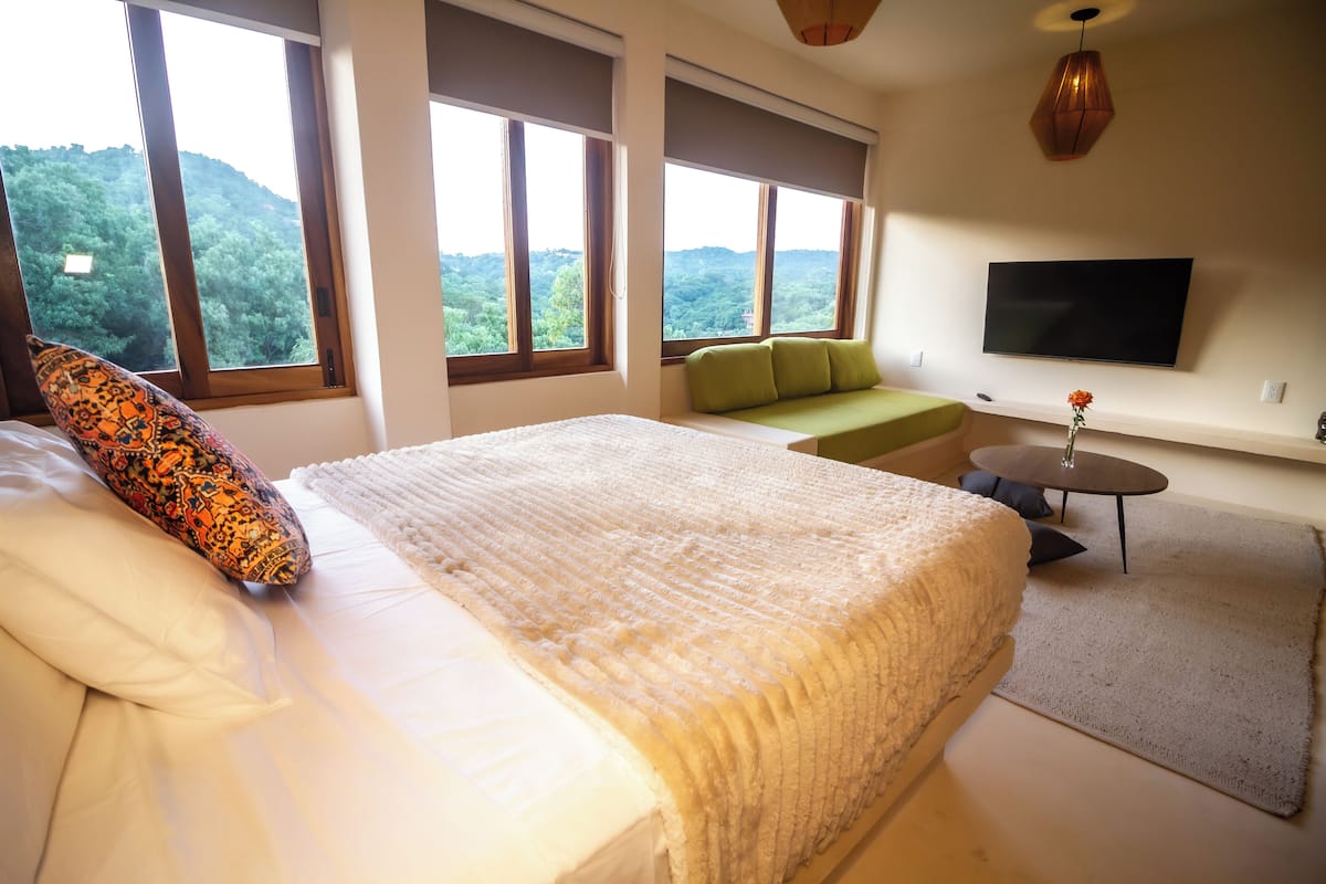 A bedroom with a large bed, a green sofa, a TV, and a view of the outdoors.