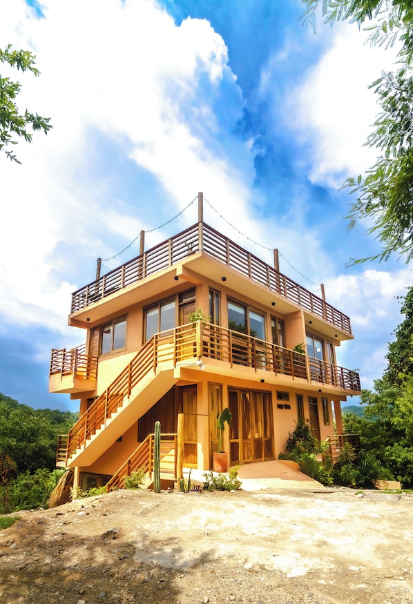 Un edificio de dos pisos con un balcón de madera, una escalera y un gran ventanal.