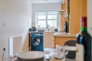 A compact kitchen with a washing machine, a window, and a countertop with various items. - Stunning 1 Bed Flat, Perfect for Business in Crewe (Cheshire East)