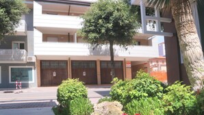Un edificio a più piani con balconi, una palma e una roccia in primo piano.