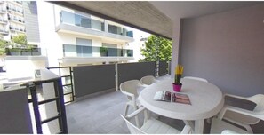 Ein Balkon mit rundem Tisch, Stühlen und einem Blumentopf.