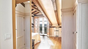 A room with a sloped ceiling, wooden beams, a bed, a table, and a chair.