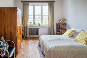 A bedroom with a bed, a wooden wardrobe, a chair, a window with curtains, and a radiator. - Lucky 13! Stunning 2 bdr apt, TOP location! (Kraków)