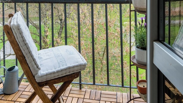 Eine Holzterrasse mit gepolstertem Stuhl, einem Blumentopf und einem Metallgeländer.