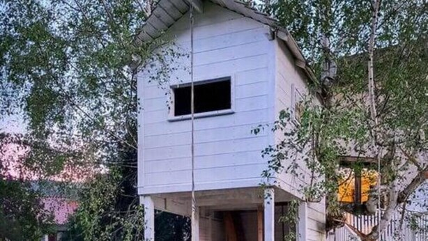 A white wooden house with a porch, a small window, and a staircase leading to the entrance.
