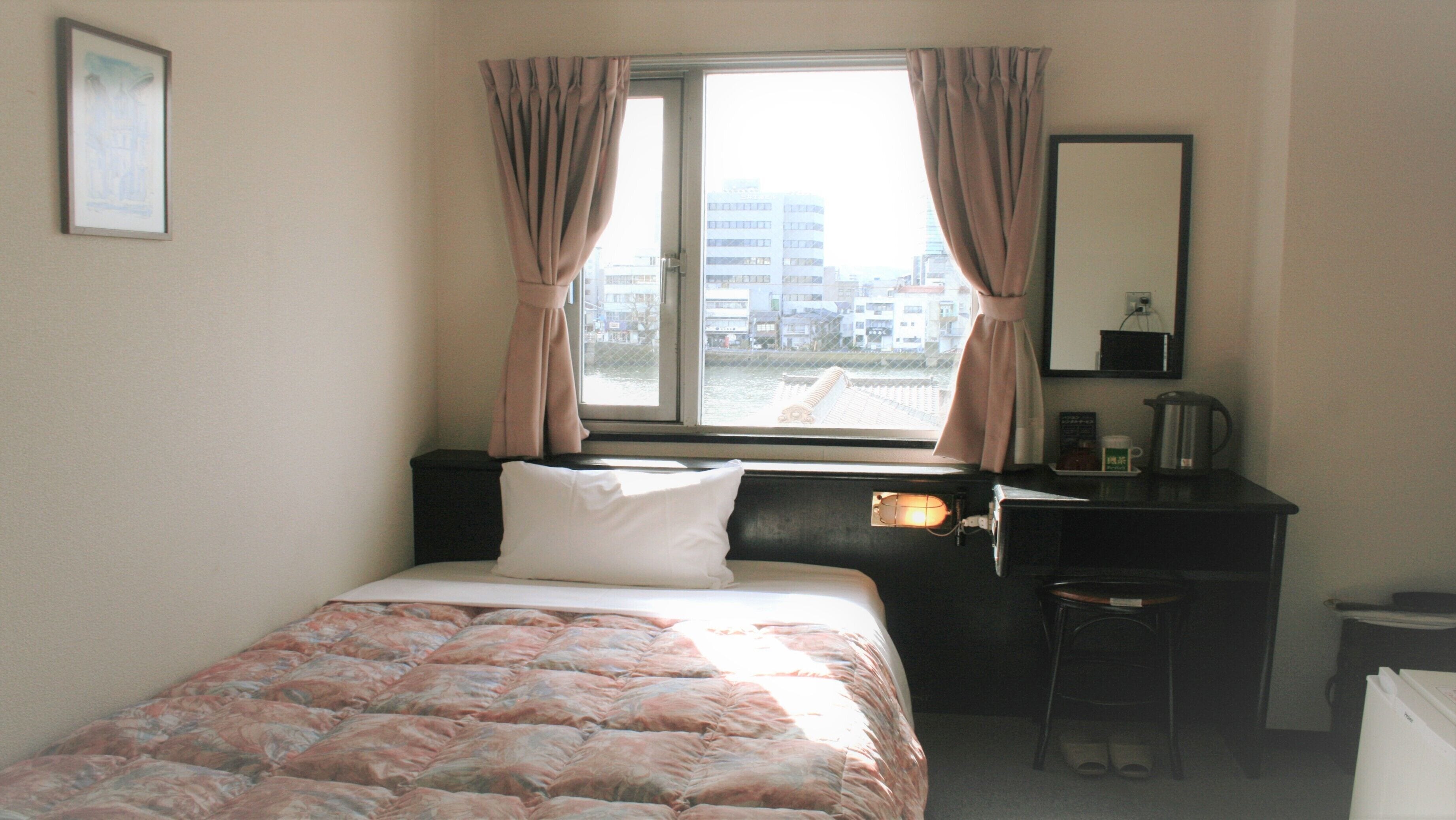 Une chambre à coucher comprenant un lit, un bureau, une chaise, une fenêtre avec des rideaux et une vue sur la ville.
