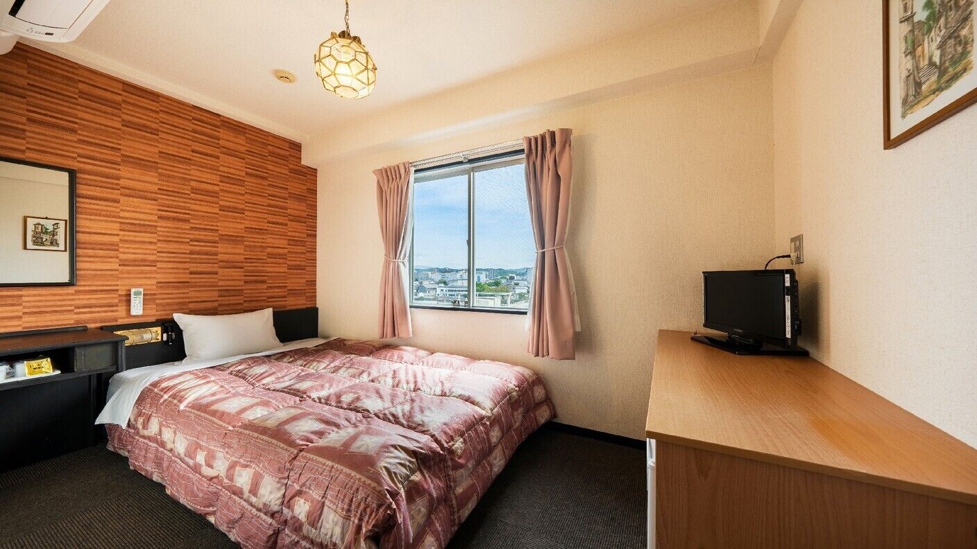 Une chambre d’hôtel avec un lit, un bureau, une télévision, une fenêtre avec des rideaux et une vue sur la ville.