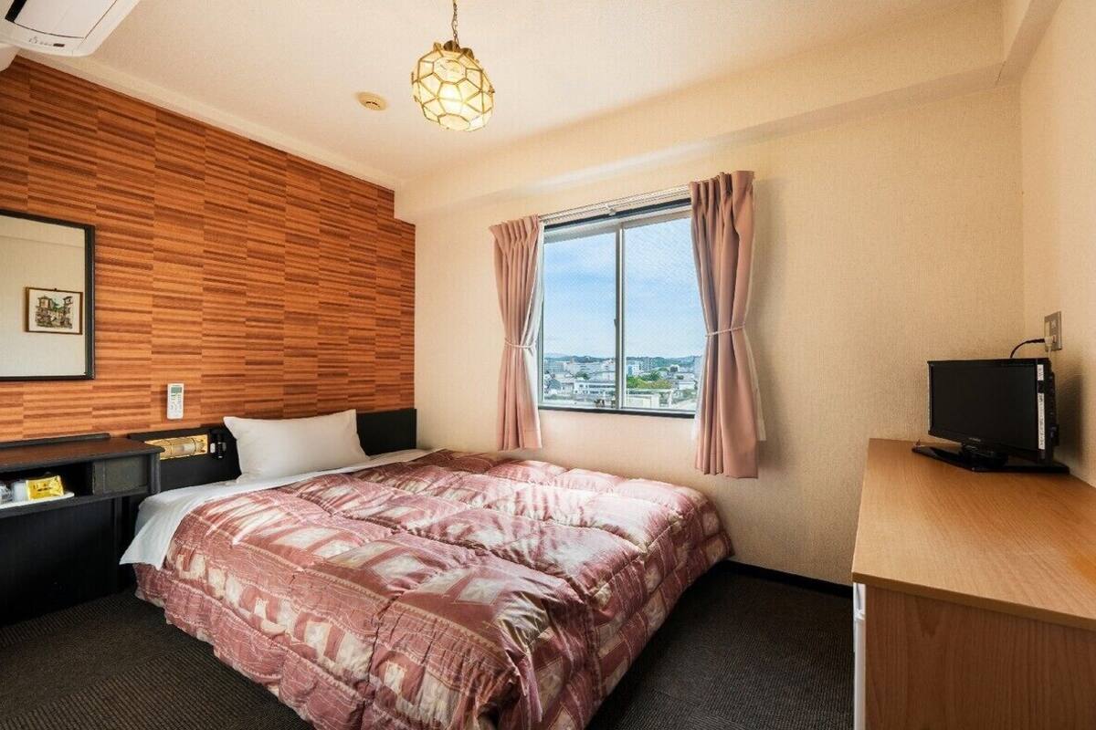 A hotel room with a bed, a desk, a television, a window with curtains, and a view of the city.