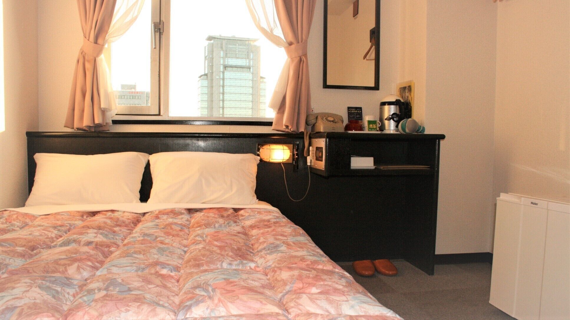 Une chambre d’hôtel avec un lit, un bureau avec un téléphone, une lampe et un radiateur.