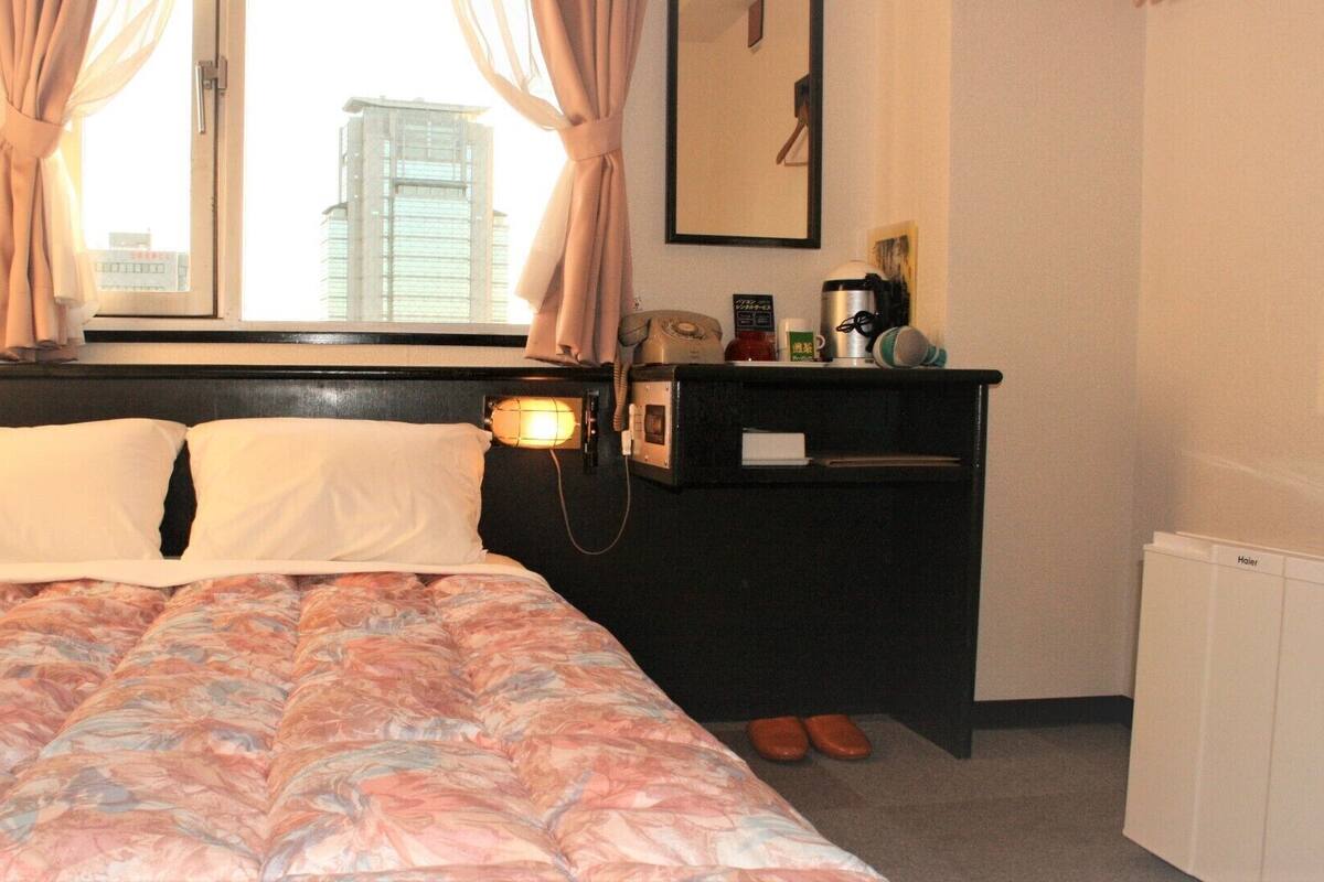 A hotel room with a bed, a desk with a telephone, a lamp, and a radiator.